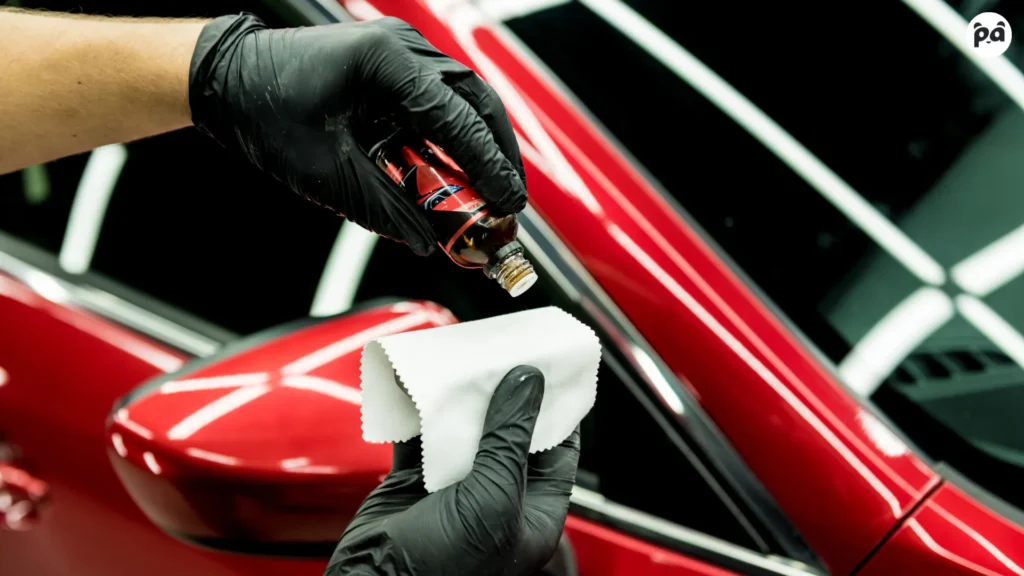 Applying ceramic coating on a red car. Factors influencing car detailing costs include materials and labor.