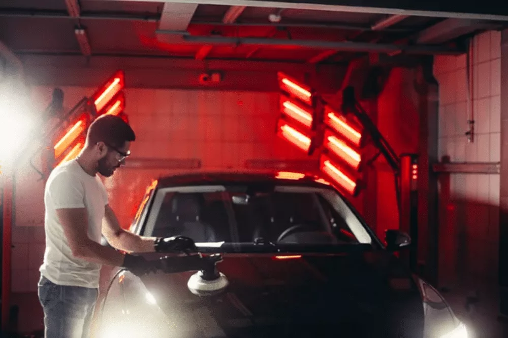 Man detailing car in garage with red lights, highlighting issues from skipping regular car maintenance.