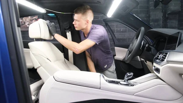 Person practicing DIY car interior detailing tips, cleaning a vehicle's light-colored seats with precision.