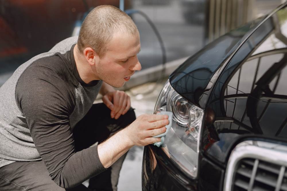 Person detailing a car headlight with a cloth, demonstrating car detailing best practices for shine and clarity.